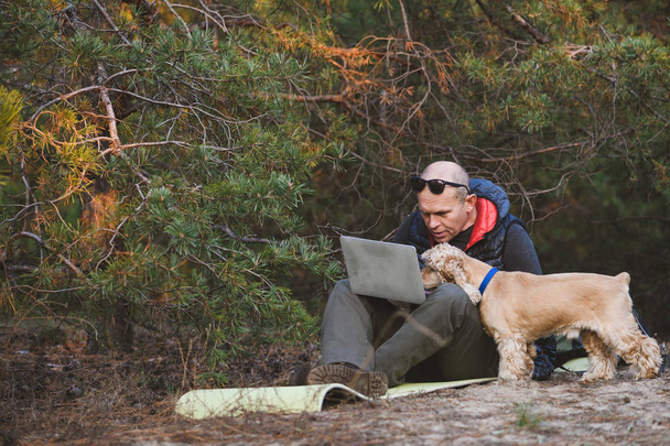 Человек и собака смотрят ноутбук на открытом воздухе
 - Фото, изображение