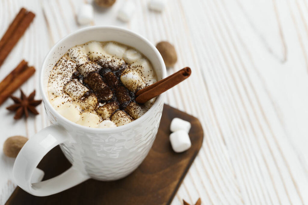White mug with hot chocolate and marshmallows with cinnamon stick on a wooden table. Hot winter drink, top view. - Foto, afbeelding