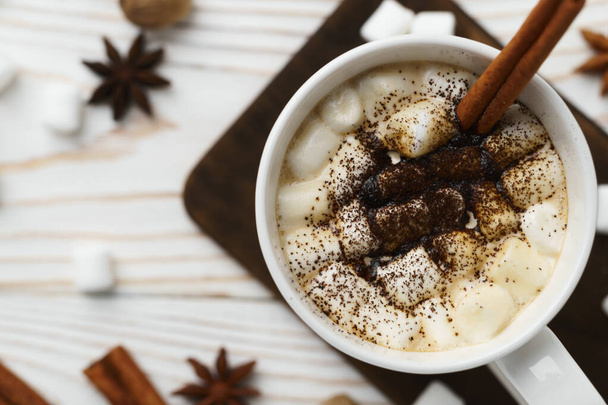 Witte mok met warme chocolademelk en marshmallows met kaneelstokje op een houten tafel. Warme winterdrank, bovenaanzicht. - Foto, afbeelding