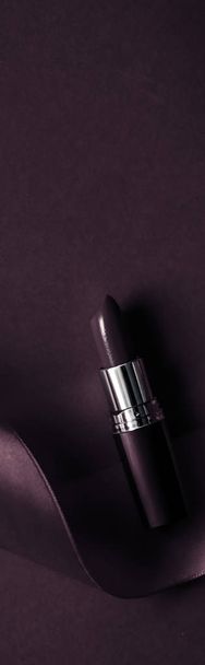 Lápiz labial de lujo y cinta de seda en el fondo de vacaciones púrpura oscuro
 - Foto, imagen