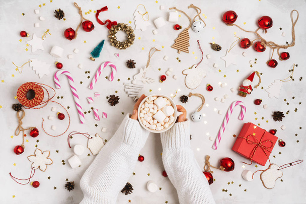 ホットチョコレート装飾されたマシュマロとカップを保持する女性の手クリスマスや新年の休日の木のおもちゃ、贈り物、ジンジャーブレッドクッキー、白を背景にヴィンテージ装飾小道具.  - 写真・画像