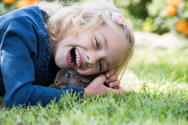 glücklich lachendes kleines Mädchen, das mit einem kleinen Hasen spielt. - Foto, Bild