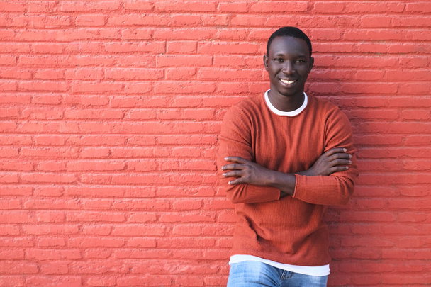 African Young Man Smiling With Red Wall In Background - 写真・画像