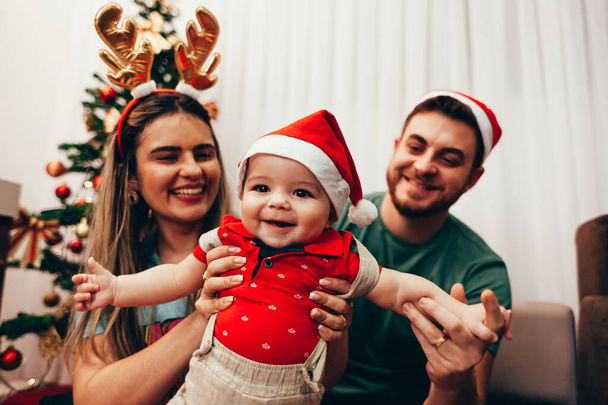 Young family celebrating Christmas at home. Happy young family enjoying their holiday time together. - Foto, Imagen