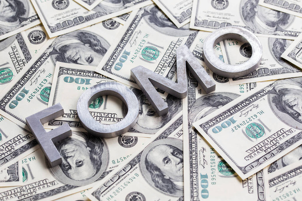 Het woord Fomo met aluminium letters op de achtergrond van de US dollar bankbiljetten - met selectieve focus - Foto, afbeelding