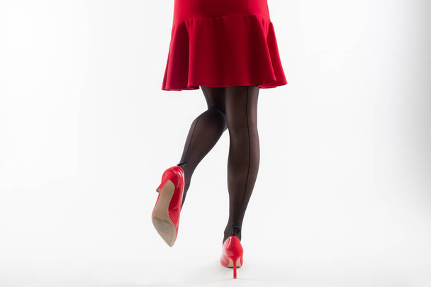 Detailní záběr na dívčí nohy v namalované punčocháče na podpatcích a v červených šatech na bílém pozadí - Fotografie, Obrázek