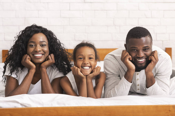Πορτρέτο της ευτυχισμένης μαύρης οικογένειας ξαπλωμένη στο κρεβάτι μαζί - Φωτογραφία, εικόνα
