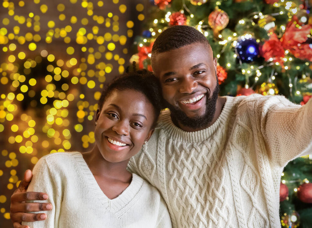 Ευτυχισμένο μαύρο ζευγάρι κάνει selfie με χριστουγεννιάτικο δέντρο στο παρασκήνιο - Φωτογραφία, εικόνα