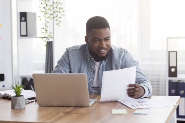 Черный бизнесмен работает с документами в офисе, проверяет финансовые отчеты
 - Фото, изображение