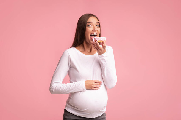 Zwangere vrouw eet donut op roze achtergrond, Studio Shot - Foto, afbeelding