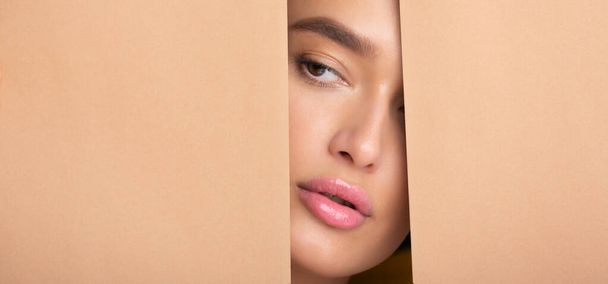 Lady with nude makeup peering into hole in peach paper - Photo, image