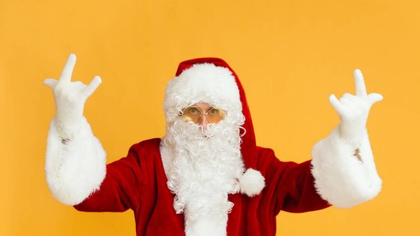 Man in Santa costume and yellow glasses showing horn sign - Foto, Bild