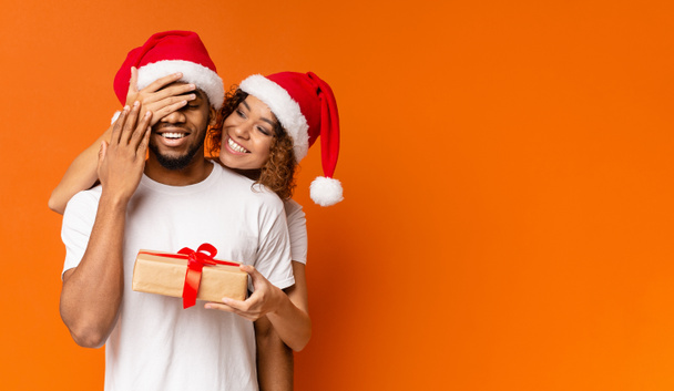 Black millennial couple with Christmas gift on orange background - Foto, afbeelding