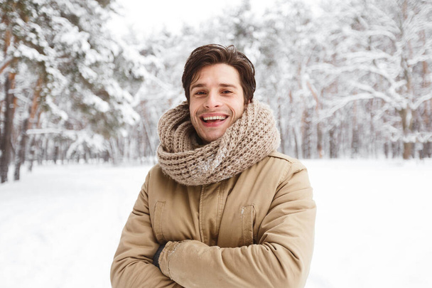 Chico sonriendo en cámara cruzando manos de pie en el bosque de invierno
 - Foto, Imagen
