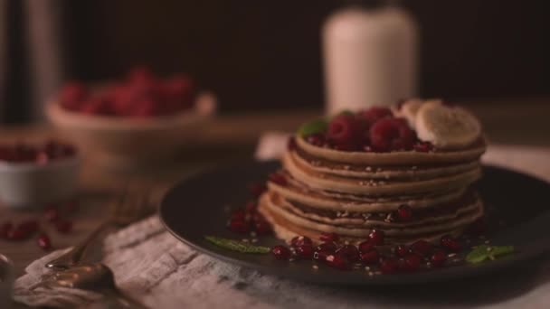 Pancakes with raspberries, banana slices, pomegranate seeds and honey on wooden vintage table. - Video