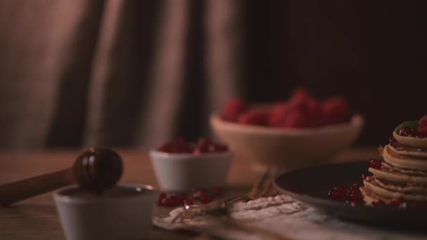 Pancakes with raspberries, banana slices, pomegranate seeds and honey on wooden vintage table. - Filmati, video