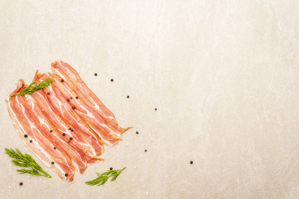 Smoked bacon slices. Raw stripes with black pepper and fresh dill on stone background, top view. - Photo, Image