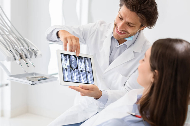 gutaussehender Arzt zeigt Patienten Röntgenbild auf digitalem Tablet - Foto, Bild