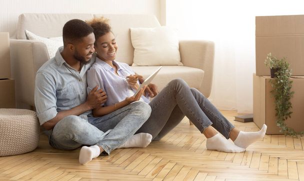 Ehepaar sitzt mit Tablet zwischen Umzugskartons im neuen Haus - Foto, Bild