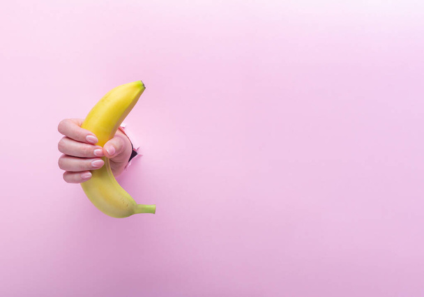 A woman holds a banana in her hand, inserted through a hole in torn paper - Foto, afbeelding