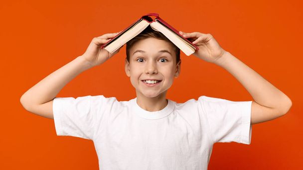 Vrolijke tiener jongen verstopt onder het dak van een boek - Foto, afbeelding