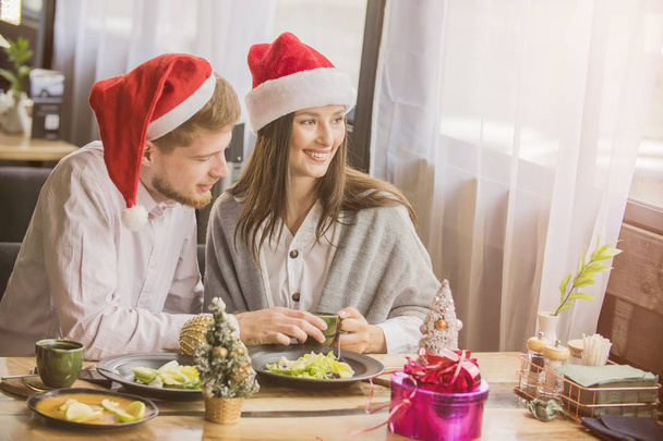 man en meisje paar vieren Kerstmis in cafe gekleed in kerst hoeden - Foto, afbeelding