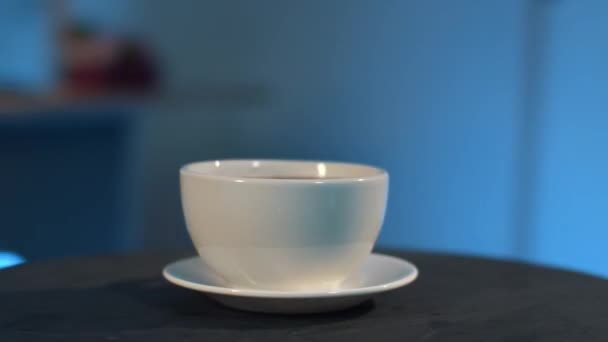 Camera revolves around white cup and saucer on black table, blue background. - Video