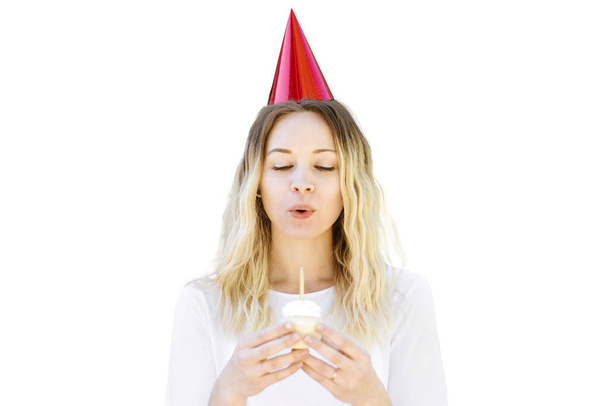 Mujer joven con sombrero de fiesta y cupcake de cumpleaños sopla sus velas
 - Foto, imagen