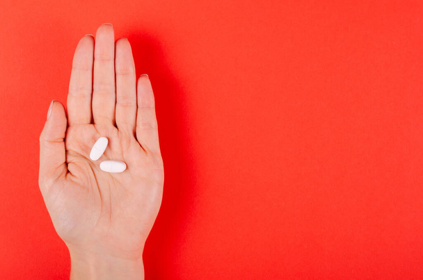 Hand with white medical pills composition on red background. - Foto, Imagen