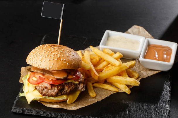 Big single cheeseburger with french fries isolated on black background. hamburger with beef patty , onion, tomato, lettuce pickles, aged cheddar, mustards, tomato jam, mayo. Horizontal - Фото, зображення