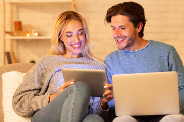 Веселі подружжя використовуючи ноутбук та цифровий планшет Websurfing вдома
 - Фото, зображення