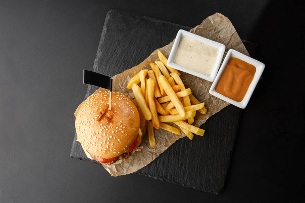 Big single cheeseburger with french fries isolated on black background. hamburger with beef patty , onion, tomato, lettuce pickles, aged cheddar, mustards, tomato jam, mayo. Horizontal - Foto, immagini