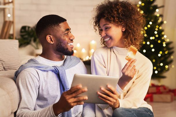 Ετοιμάζομαι για τα Χριστούγεννα. Ενθουσιασμένοι afro ζευγάρι αγοράζουν δώρα σε απευθείας σύνδεση - Φωτογραφία, εικόνα