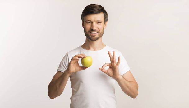 Man holding Apple Gesturing Ok álló felett fehér háttér - Fotó, kép