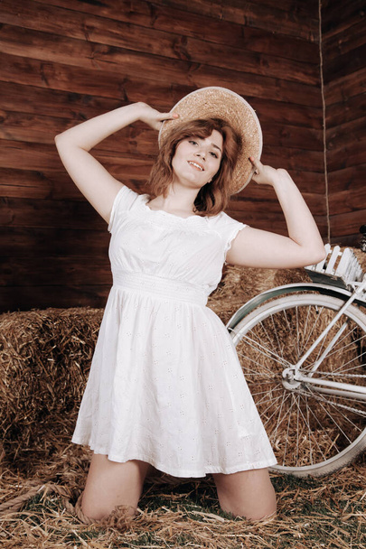 hermosa chica en un vestido de verano blanco posa con una bicicleta en el heno después de la cosecha de otoño
 - Foto, imagen