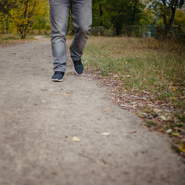 Männerbeine in Jeans und Turnschuhen gehen hinaus in die Ferne auf den Boden, der mit abgefallenen gelben Blättern bedeckt ist. Herbst-Anreisekonzept, Nahaufnahme, Kopierraum. - Foto, Bild