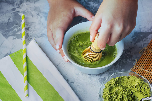 The process of making green tea matcha. Girl stirs a green drink with a bamboo whisk - Valokuva, kuva
