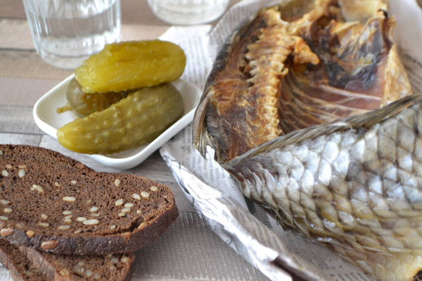Russian vodka with a stockfish and newspaper with pickled cucumber and black bread - Photo, Image