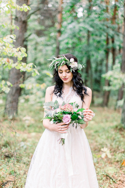 beautiful bride in nature in a coniferous forest in a wreath on her head and a luxurious wedding dress. Rustic boho style of wedding outdoors - 写真・画像