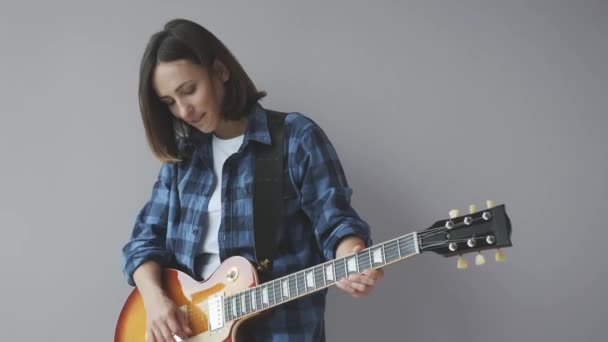 Attractive girl with electric guitar playing jazz and blues songs. Female playing guitar isolated wearing blue casual shirt. - Felvétel, videó