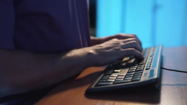 Kamera obraca się wokół rąk człowieka w fioletowym t-shircie wpisując na czarnej klawiaturze - Materiał filmowy, wideo