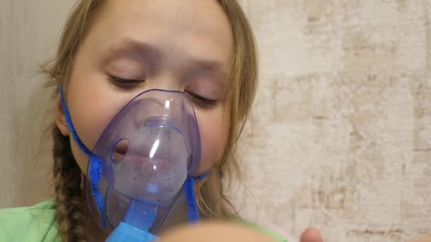 klein meisje behandeld met een inhalatiemasker op haar gezicht in het ziekenhuis. kind met een tablet is ziek en ademt via een inhalator. close-up. Peuter behandelt griep door inhalatiedamp in te ademen. - Video