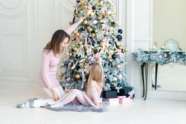 Portrét roztomilé roztomilé malé blonďaté holčičky s matkou vychutnat ořezávání vánoční stromek v útulném obývacím pokoji doma. Máma a dcera zdobí. Nový rok dovolená šťastný rodinný oslava koncept - Fotografie, Obrázek