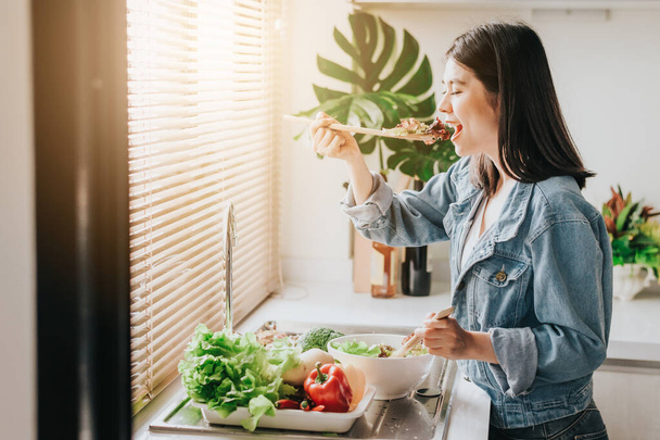Donna felice mangiare sana insalata di verdure fresche in cucina
 - Foto, immagini