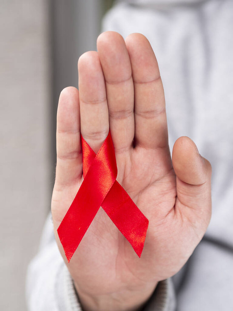 Close up of a young man holds in hand red ribbon and showing hand gesture to stop. World AIDS day concept vertical shot - Photo, Image
