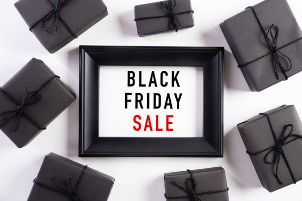 Top view of Black Friday Sale text on white picture frame with black gift box and Christmas ball and berries on white background. Shopping concept and black Friday composition. - 写真・画像