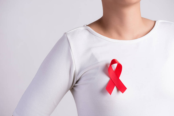 Nahaufnahme einer roten Schleife auf der Brust einer Frau zur Unterstützung des AIDS-Tages. Gesundheitswesen, Medizin und AIDS-Aufklärungskonzept. - Foto, Bild