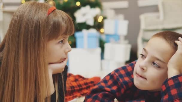 Closeup 4k video of cute little kids spend pleasant time together, communicating on the carpet near Christmas tree. - Imágenes, Vídeo