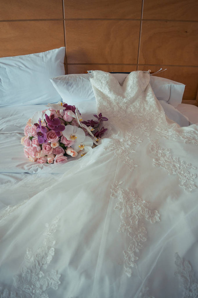vestido de novia sobre la cama, con el ramo de flores - Фото, изображение