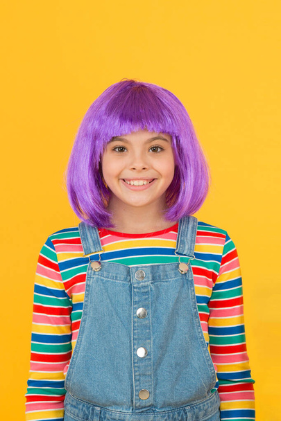 Being fancy child. Small child wear violet hair wig yellow background. Happy child with straight short hairstyle in casual style. Cute little child smile with fashion look - Foto, Imagen